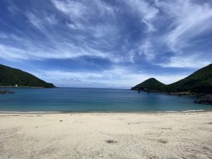 湾の左右から緑の山が迫り、白い砂浜が広がり、青い海と空が広がる穏やかな景色の写真
