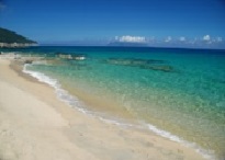 白い砂浜に透明度の高いエメラルドグリーンの海水が寄せ、遠くには島影がかすむ、南国らしい海岸の風景写真