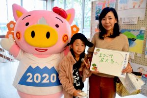 施設内で、母親と子供が手書きのスケッチブックを掲げ、豚のキャラクターの着ぐるみと並んで撮影した写真