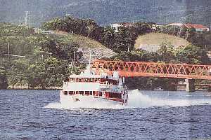 赤い鉄橋を背景に、白と赤の高速船が水しぶきを上げながら進んでいるトッピーの写真