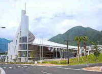 白い近代的な建物が道路沿いに立ち、特徴的な尖塔状の構造を持った屋久島環境文化村センターの外観写真