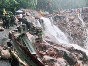 豪雨により土砂崩れが起き、道路やガードレールが崩壊し、水が滝のように流れている災害現場の写真