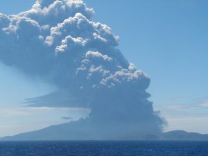 口永良部島が噴火し、灰色の噴煙を上げている様子を海を挟んで撮影した写真