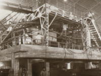 鉄骨とコンクリートで組まれた大型の産業用構造物が屋内に設置され、複雑な配管や階段が取り付けられた工場設備の写真