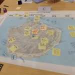 大な地図の上に、書き込みがされた黄色の付箋がたくさん貼り付けられている写真