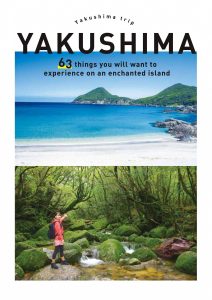 上部に青い海と空、白い砂浜、緑の山々が広がる海岸線の写真、下部に苔むした緑の岩が連なる沢に立つ赤いジャケットと黒いバックパックの女性の全身写真が配置され、「Yakushima trip」「YAKUSHIMA」「63 things you will want to experience on an enchanted island」の文字が入った旅行ガイドブックの表紙（屋久島観光パンフ【英語版】のサイトへリンク）