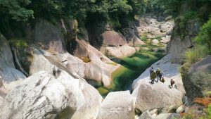 巨大で滑らかな白い岩石が幾重にも重なる渓谷の中を、透き通ったエメラルドグリーンの川が穏やかに流れ、岩の上に数人の人々が登っている様子の写真
