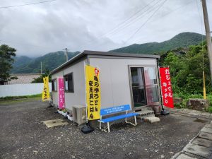 建物の前には、黄色や赤色ののぼり旗が複数立てられており、それらの旗には料理名が書かれている店構えの写真