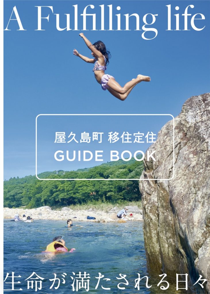青い空と海、切り立った岩場の下の水辺で泳ぐ人々、上空で飛び込み台から水面へ向けて両手を広げて飛び跳ねる水着姿の少女を捉え「A Fulfilling life 」「屋久島町 移住定住 GUIDE BOOK 」「生命が満たされる日々」というテキストが記載された屋久島町の移住定住ガイドブックの表紙の写真