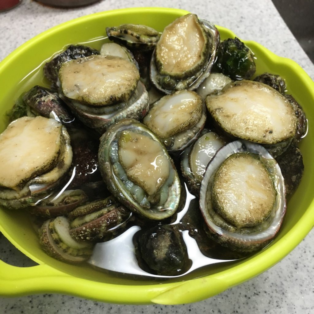 水を張った黄緑色のボウルにたくさんの殻付きのトコブシが入っている写真