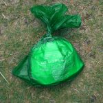 芝生の上に緑色の防水袋が中身を包むようにしっかり結ばれ、袋表面には白文字で説明が印字された携帯トイレの廃棄物処理後の状態を示す写真