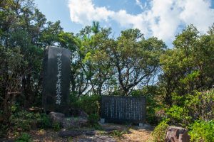 深緑の木々に囲まれた場所に、黒い長方形の石碑と横長の石板が並んで立っており、長方形の石碑には「神父シドッチ上陸記念碑」と日本語で刻まれている、記念碑の写真