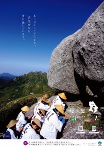突き抜けるような青空の下、岩がゴロゴロ転がる山頂で、白い法被に笠をかぶった一行が巨大な花崗岩のそばで両手を合わせ岩に向かってお祈りをしているポーズをとっており、「ありがとうございす。この気持ちを受け継いでいます。」というメッセージと「屋久島 YAKUSHIMA」の文字が重ねられた観光ポスターの写真