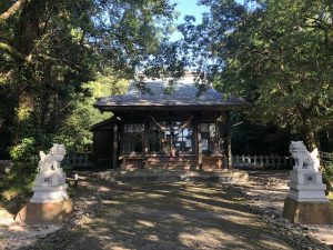 木々に囲まれた境内の中央に、木造の小さな拝殿が建っており、その左右には白い石造りの狛犬が置かれ、神社の厳かな雰囲気が感じられる写真