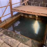 トタンとコンクリートブロックで囲まれた長方形の湯船を上から捉えた写真で、湯船は石垣で囲まれ、一部が木の板で覆われている露天風呂全景写真