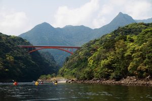 緑の山間に架かった赤い愛ー千葉市の下を流れる川に複数のカヤックが浮かんでいる写真