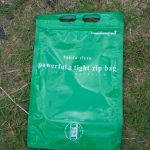 芝生の上に置かれた緑色の防水性ジッパーバッグで、中央に白文字で「powerful ＆ tight zip bag」と印字され、上部には持ち手用の穴が二つ並ぶ携帯用密閉袋の写真