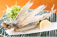 トビウオの姿揚げが1つ、レモンと野菜を添えた黒と白のストライプ模様の皿に盛りつけられている写真