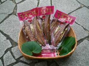 石畳の上に置かれた竹籠の中に、赤いラベルが付いた屋久島特産の鯖節の真空パックが3袋並べられている写真