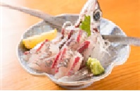 長いひれが皿から飛び出した尾頭付きのトビウオの刺身が、レモンとワサビを添えて皿に盛りつけられた写真