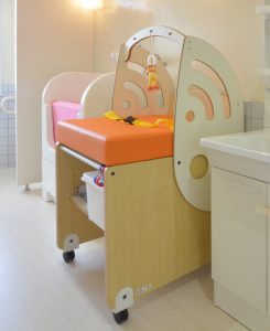 オレンジ色のマットが付いた、キャスター付きの木製のオムツ交換台が、洗面台の横に配置されている写真